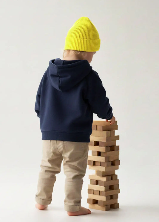 Kleinkind mit J.Clay Kids Beanie Lemon stapelt Klötze, stehend und von der Kamera abgewandt.