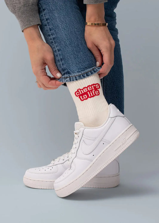 Person in Jeans und Sneakern zeigt Cheers to life Socken aus Baumwolle von J.Clay.