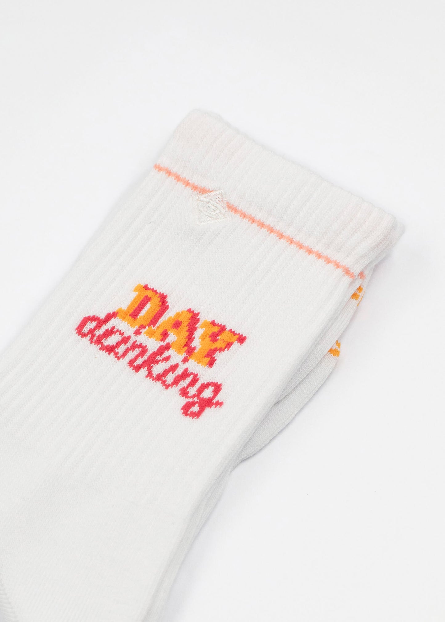 Ein Paar weiße J.Clay Tennissocken mit orangefarbenem und rotem "DAY drinking"-Text auf der Seite, der auf weißem Hintergrund gestrickt ist.