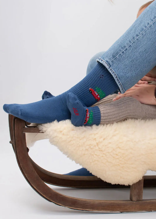 Zwei Personen in Socken und Jeans auf einem Holzschlitten mit weißem Fell, dazu läuft „Driving Home for Christmas“ von J. Clay.