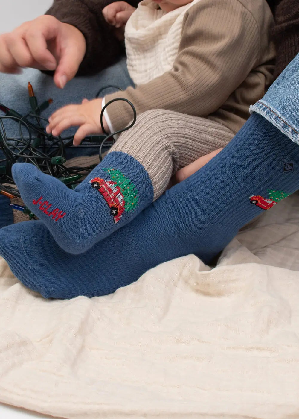Erwachsener und Baby in „J.Clay Driving Home – Fam Pack“-Socken mit Auto- und Baummotiven auf einer Decke.