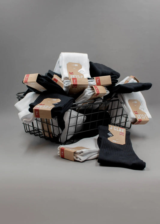 J.Clay Essential Pack Drahtkorb mit schwarzen und weißen Socken auf grauem Hintergrund.