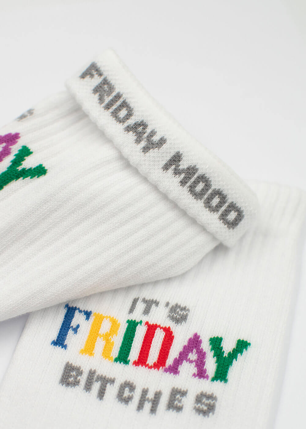 Ein Paar weiße J.Clay-Tennissocken mit gerippten Oberteilen, auf denen "ITS FRIDAY BITCHES" in fetten, bunten Buchstaben in der Nähe des Oberteils aufgestickt ist.