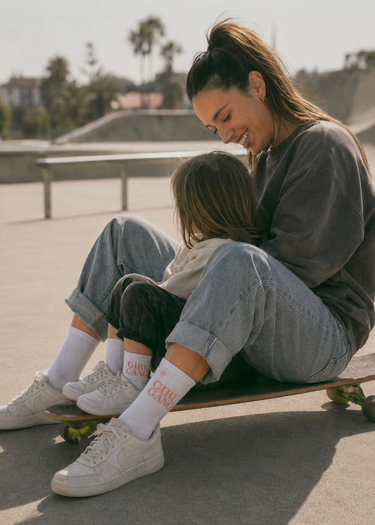 Mutter und Kind, beide im „Girl Gang – Fam Pack“ von J.Clay, lächeln gemeinsam im Skatepark.