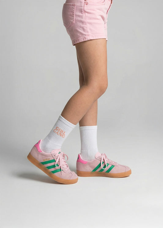 Person in rosa Shorts, J.Clay Girl Gang - Kids Socken und rosa Adidas Turnschuhen mit grünen Streifen.