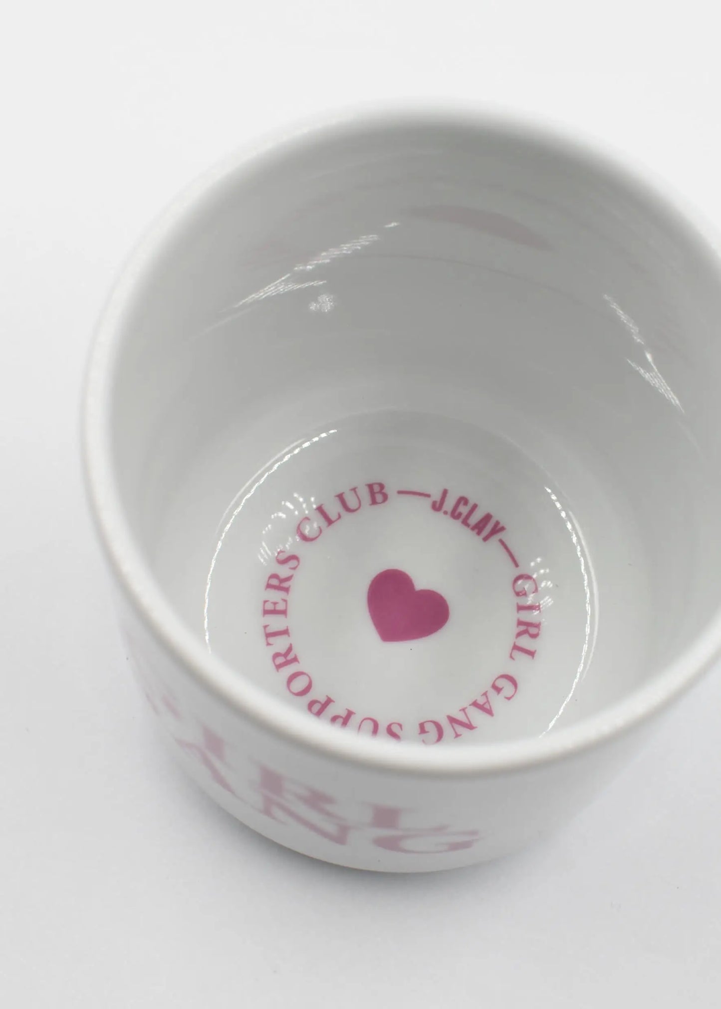 Eine weiße Keramik J.Clay Tasse ohne Henkel von oben gesehen, mit einem rosa Herz und "SUPPORTERS CLUB - J.Clay - GIRL GANG" in einem Kreis auf dem inneren Boden.