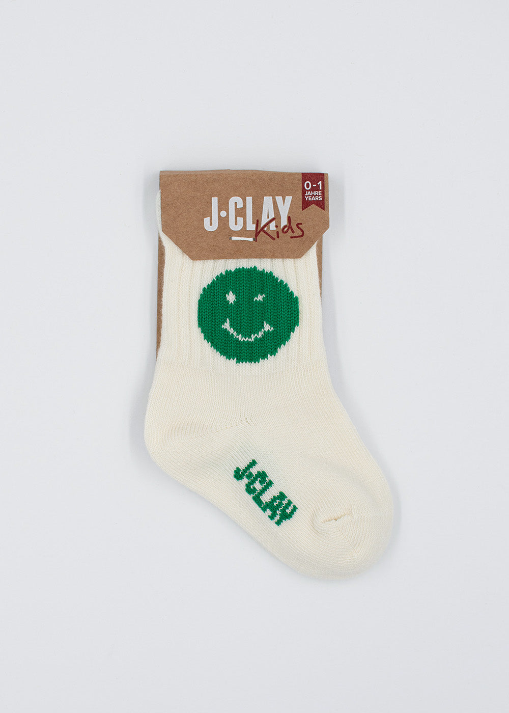 J.Clay Green Smile – Beigefarbene Mini-Babysöckchen mit grünem Smiley, in einer Kartonverpackung.
