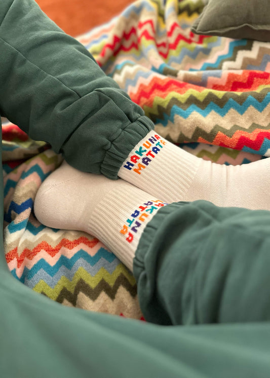 Ein Paar weiße J.Clay Tennissocken mit der Aufschrift "Hakuna Matata" in bunten, verspielten Buchstaben an der Oberseite.