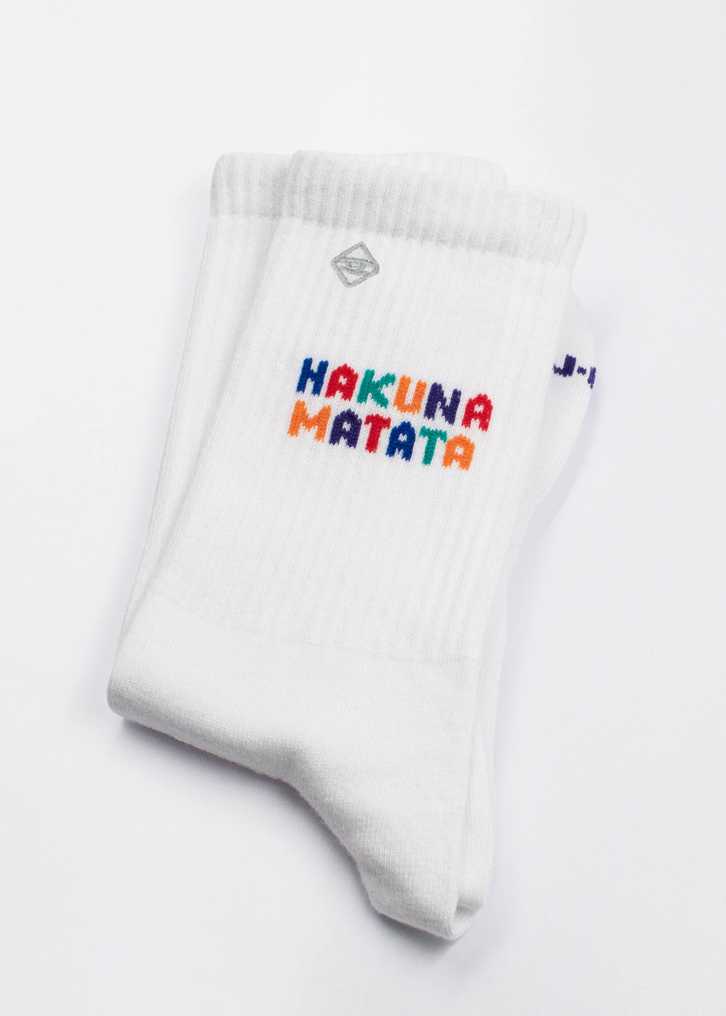 Ein Paar weiße J.Clay Tennissocken mit der Aufschrift "Hakuna Matata" in bunten, verspielten Buchstaben an der Oberseite.
