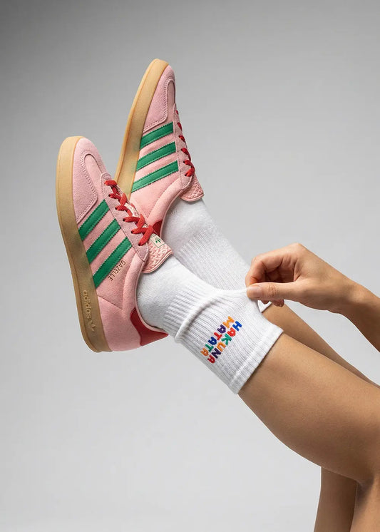 Person trägt pinke Adidas mit grünen Streifen und J.Clay Hakuna Matata Tennissocken.