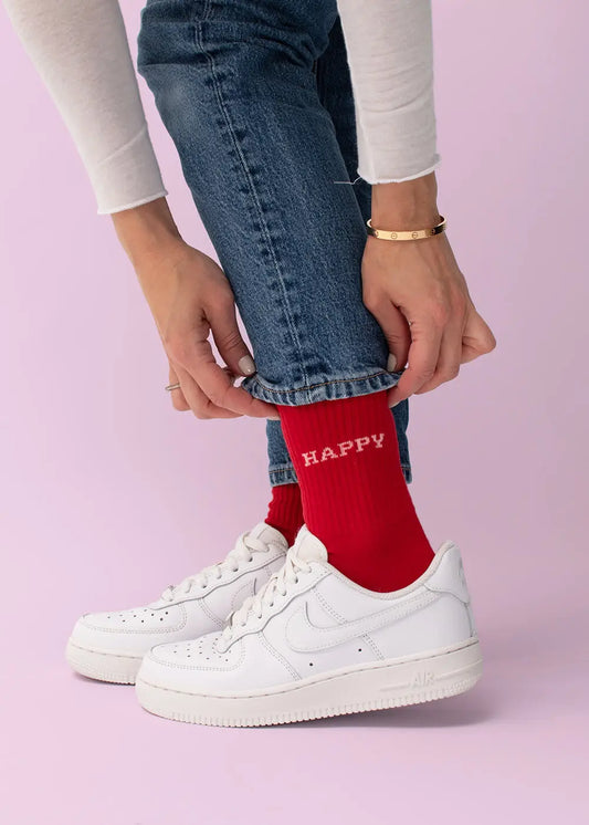 Person in J.Clay Happy Tennissocken und weißen Turnschuhen, die ihre Jeansmanschette zurechtrückt.