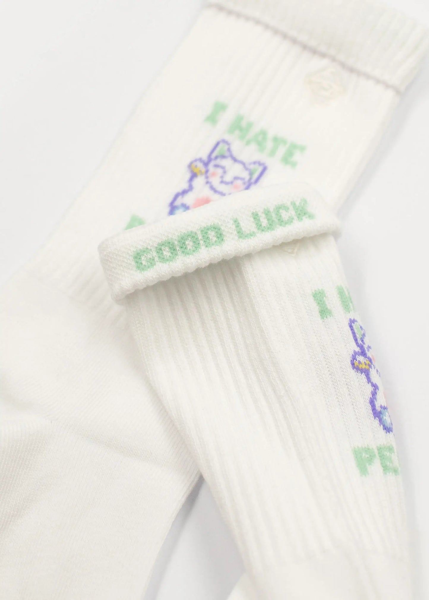 Weiße Tennissocken von J.Clay mit grünem "I HATE PEOPLE"-Text und einer winkenden Katzenillustration; die umgeschlagene Manschette enthüllt den versteckten "GOOD LUCK"-Text.