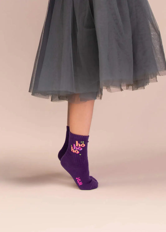 Ein Kind in einem durchsichtigen grauen Rock steht auf Zehenspitzen und trägt die lila „Ho ho ho“-Socken von J.Clay.