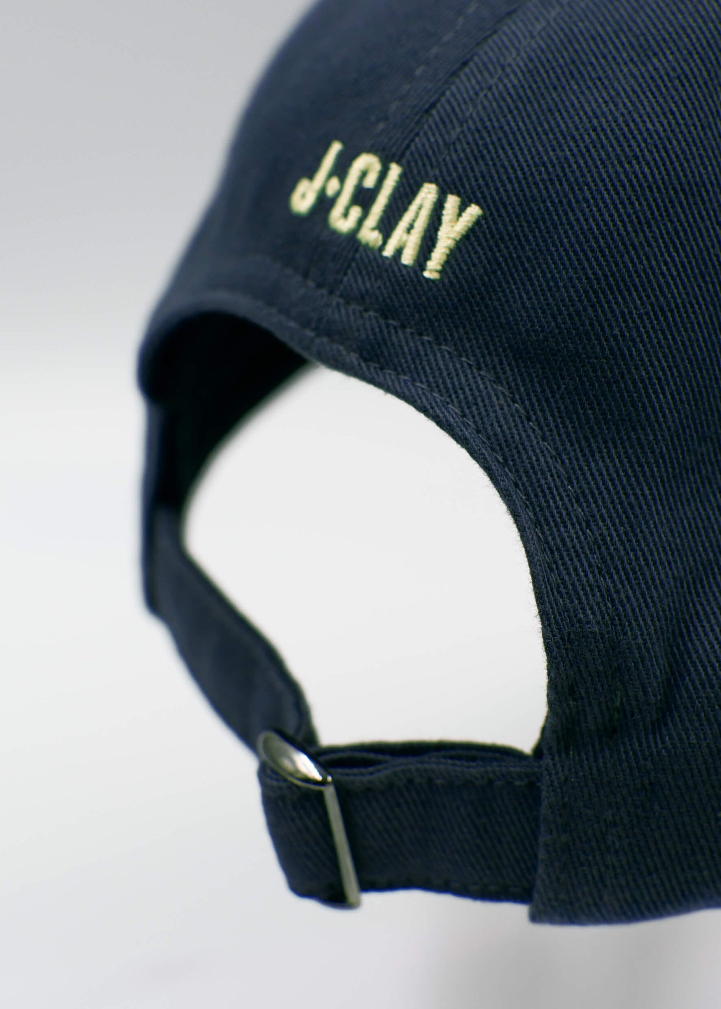 Nahaufnahme der Rückseite einer marineblauen J.Clay Dad Cap mit verstellbarem Riemen und Metallverschluss, auf der über der Öffnung "J.Clay" eingestickt ist.