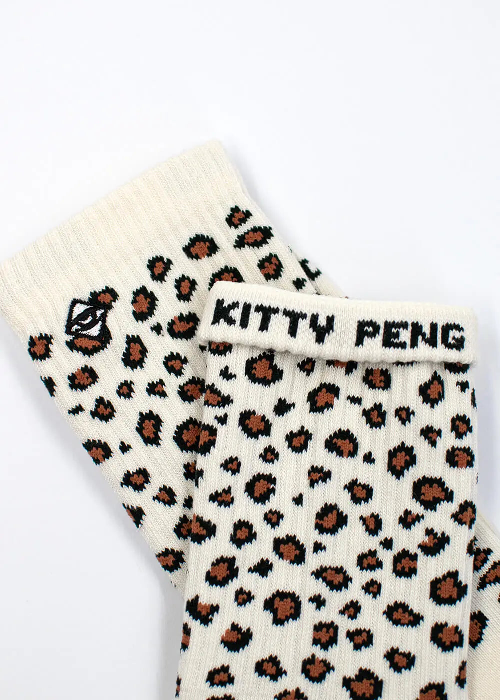 Die cremefarbenen J.Clay Leo Tennissocken sind mit einem braunen und schwarzen Leopardenmuster versehen. Eine Socke ist gefaltet und zeigt den Text "KITTY PENG" und ein kleines gesticktes Katzengesicht in der Nähe des Bündchens.