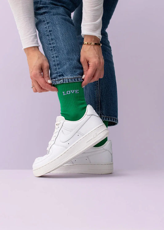 Person in Jeans und weißen Sneakern zeigt J.Clay Love Tennissocken, in Deutschland designt.