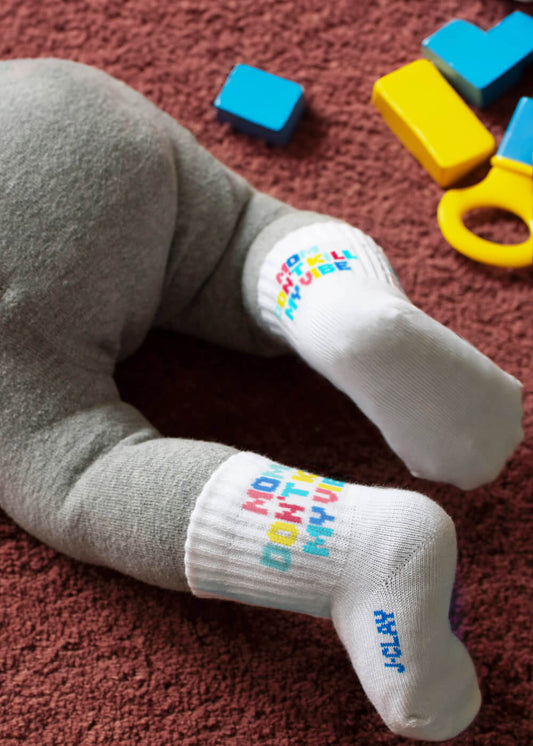 Zwei Paar weiße J.Clay-Socken - ein Paar für Erwachsene ("Mama Kind Socken") und ein Paar für Kleinkinder - für einen lustigen Partner-Look! Beide haben einen bunten Text, ein rotes, quadratisches Logo und das Paar für Erwachsene hat gerippte Bündchen mit lila Abschlüssen. - Mama Kind Packs