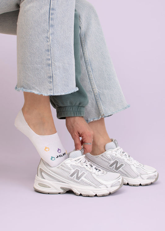 Jemand in Jeans trägt weiße New Balance Sneakers und J.Clay Nice Day Füßlinge.