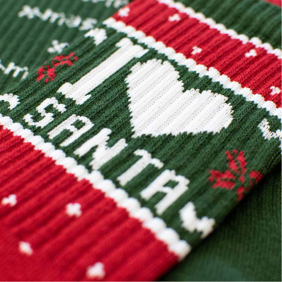 Nahaufnahme eines gestrickten Weihnachtspullovers mit einem rot-grün-weißen Muster, auf dem "I ♥ Santa" steht, mit Schneeflocken und Rentiergeweih als dekorative Akzente.