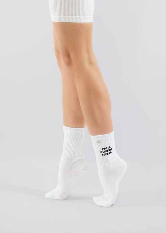 Eine Person trägt weiße gerippte Shorts von J.Clay und weiße Tennissocken mit dem fetten schwarzen Text "IM A F*CKING NINJA" und steht auf Zehenspitzen vor einem einfachen hellen Hintergrund.