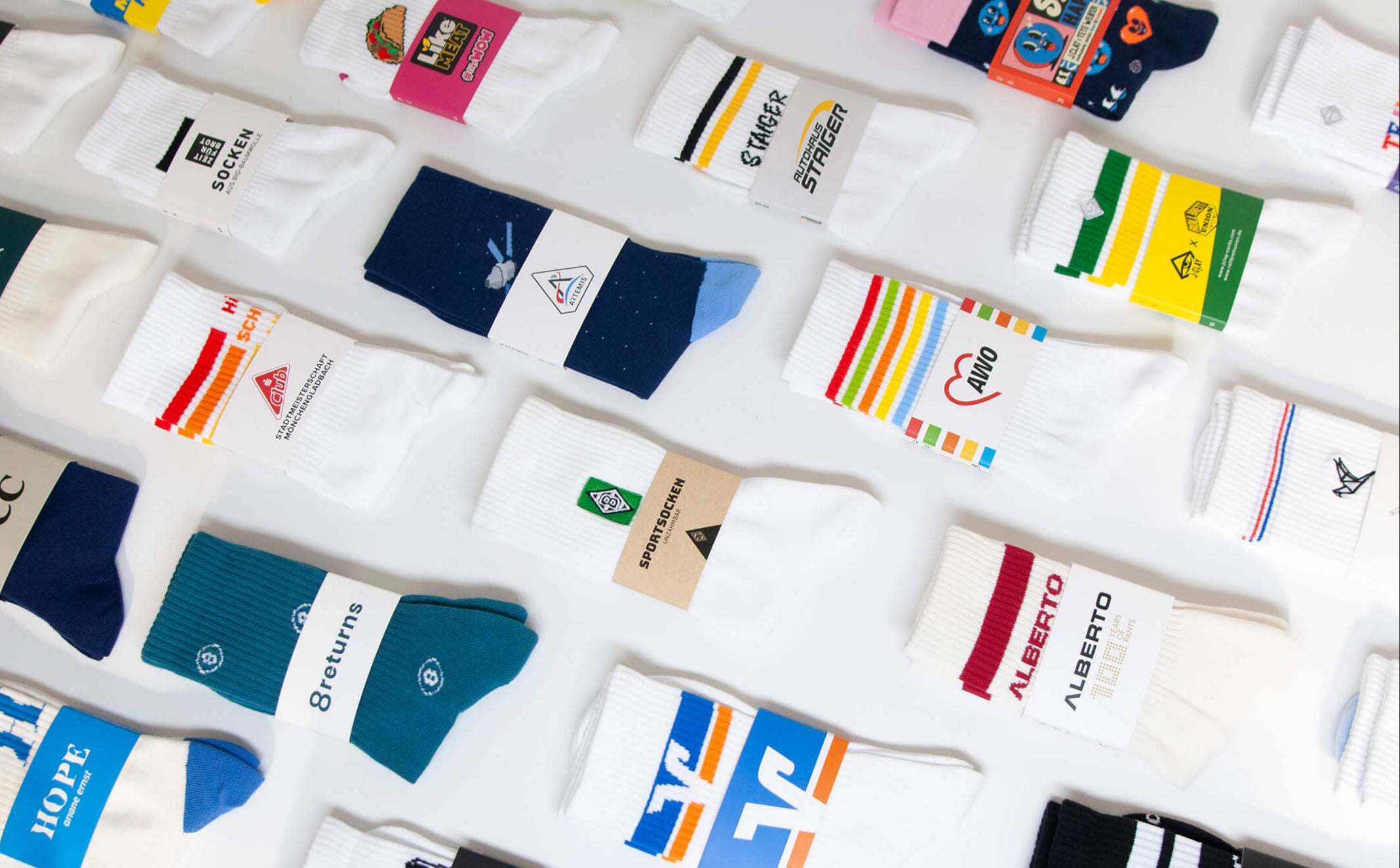 Eine Vielzahl von bunten Socken, jede mit einzigartigem Design und Branding, sind ordentlich in Reihen auf einer weißen Oberfläche angeordnet. Einige Socken weisen Streifen, Logos und Text in verschiedenen Farben auf.
