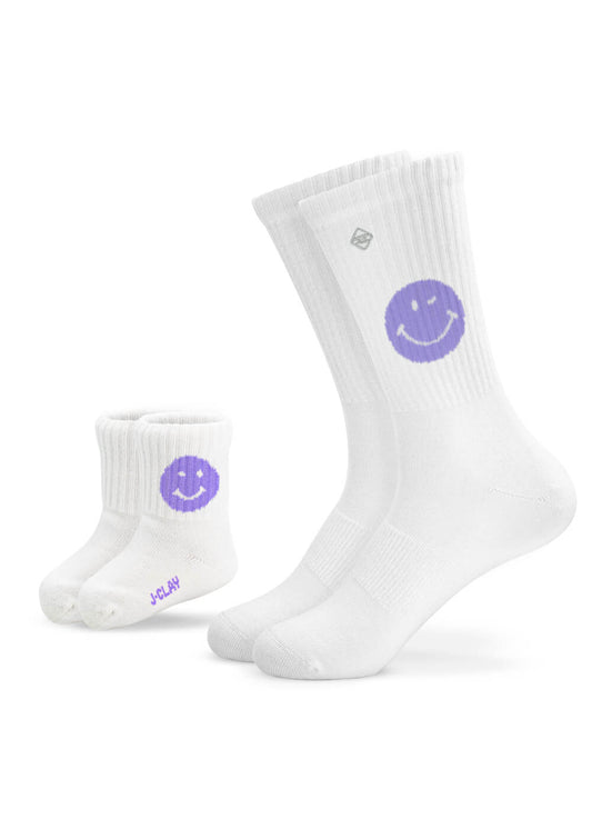 Zwei Paar weiße J.Clay-Socken - ein Erwachsener, ein Baby - jeweils mit einem lila Smiley-Gesicht. Perfekt für Partner-Look oder Mini Me Momente! Auf den Babysocken steht "J.Clay" in lila in der Nähe der Zehen. - Mama Kind Packs