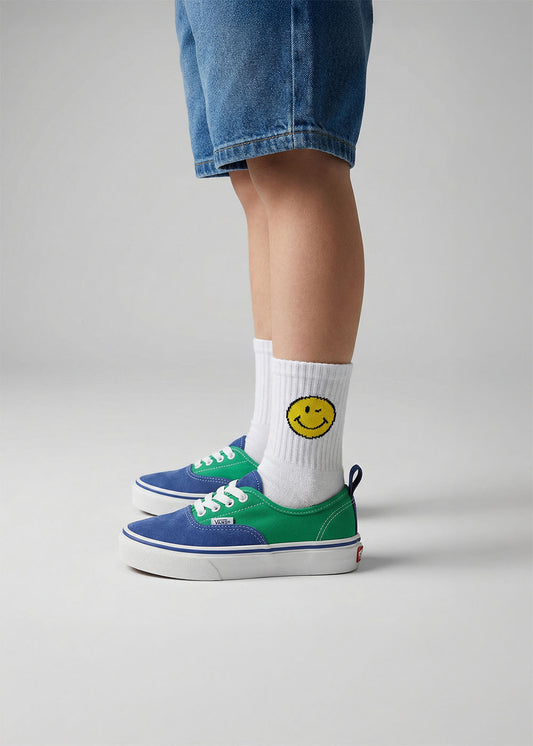 Das Kind trägt blau-grüne Turnschuhe, Yellow Smile - Kindersocken von J.Clay und Denim-Shorts.
