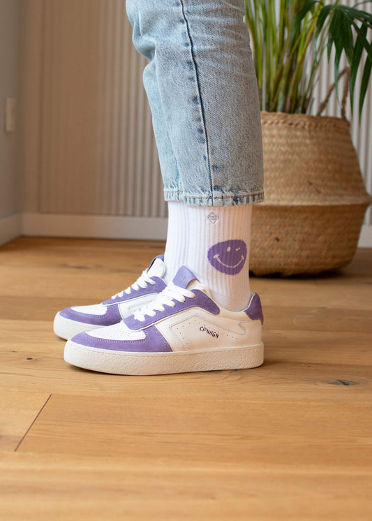 Ein Paar weiße J.Clay Tennissocken mit einem lilafarbenen Smiley an der Spitze und einem kleinen quadratischen Logo über dem Knöchel, die aufrecht auf einem schlichten weißen Hintergrund stehen. - Tennissocken