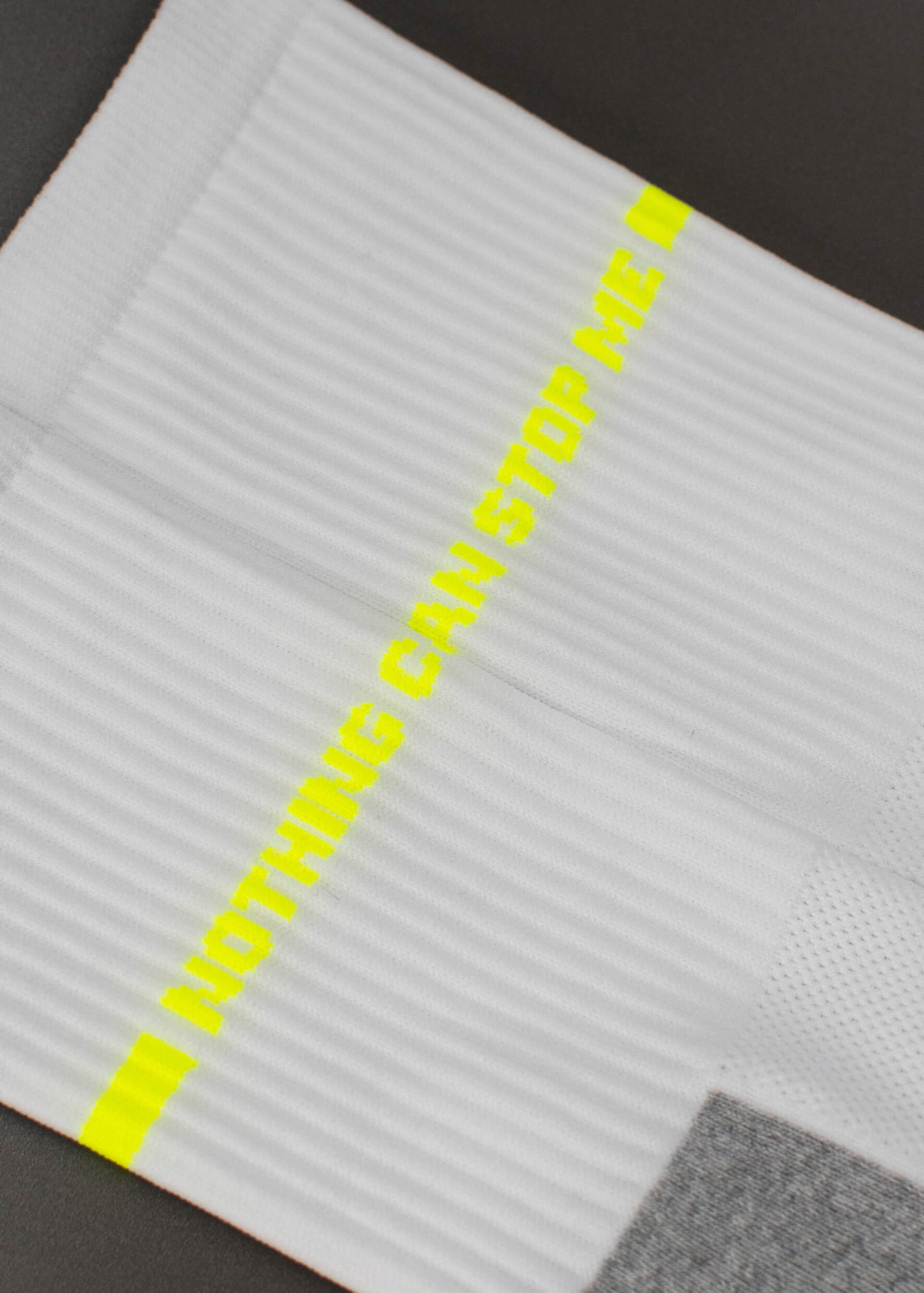 Eine Nahaufnahme einer weißen gerippten Sportsocke von J.Clay mit dem Schriftzug "NOTHING CAN STOP ME" in gelben Großbuchstaben und aus atmungsaktivem Material für hohen Tragekomfort.