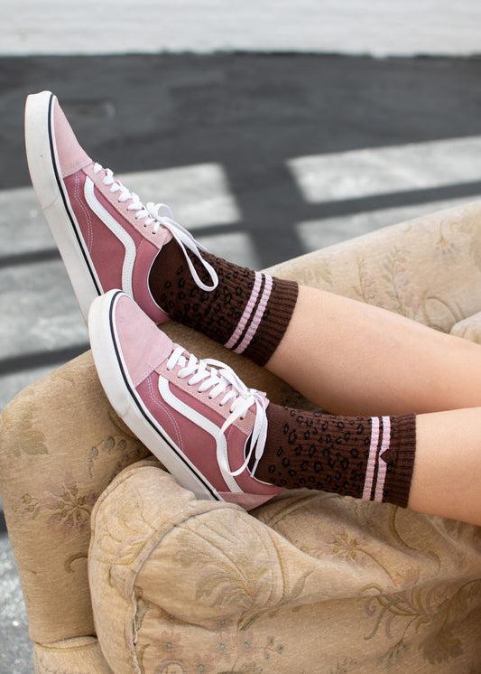 Glitzernde „Leo“-Sneaker von J.Clay mit weißen Schnürsenkeln und braunen, gepunkteten Socken auf einem beigen Sofa.