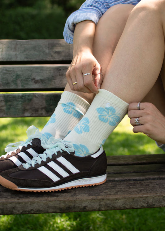 Person trägt J.Clay Hibiscus Flower Socken und schwarze Adidas Turnschuhe auf einer Holzbank im Freien.