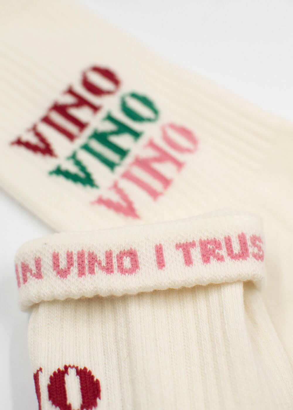 Cremefarbene Tennissocken von J.Clay mit dreifach gesticktem "VINO" in Rot, Grün und Pink. Auf dem Sockenbündchen ist der Satz "IN VINO I TRUST" in Rosa aufgestickt.