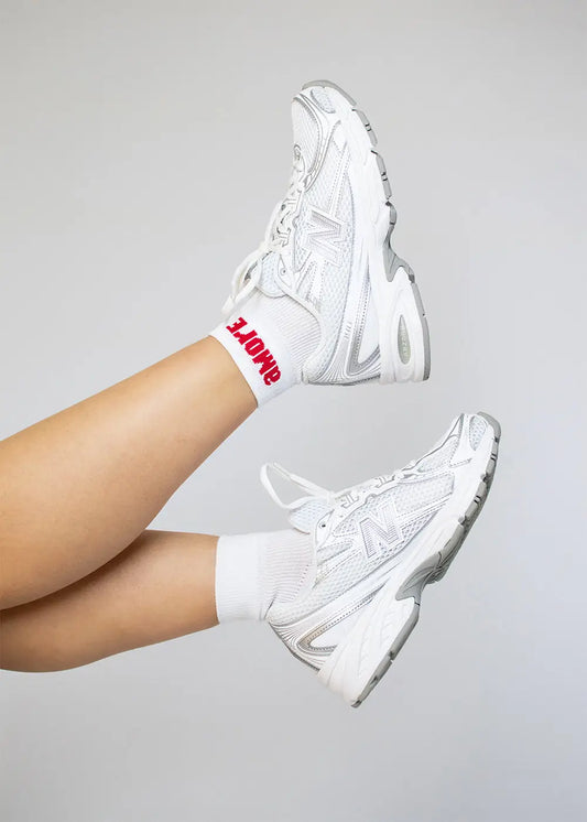 Zwei Beine in J.Clay Amore Sneaker Socken High, eine Socke zeigt roten AMORE-Schriftzug.