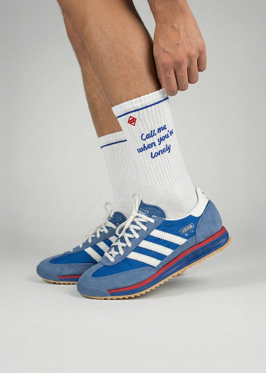 Person trägt blaue Adidas-Turnschuhe und J.Clay Call Me weiße Socken.