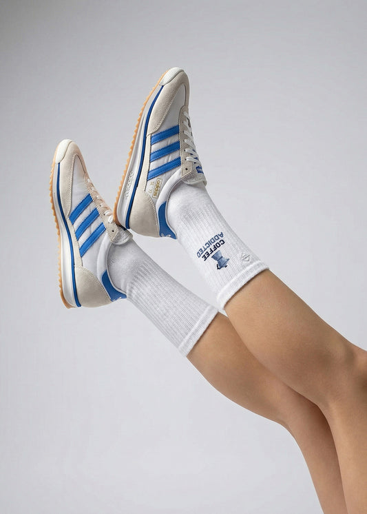 Person mit J.Clay Coffee Addicted Socken und weißen Turnschuhen mit blauen Streifen, Beine hochgelegt.