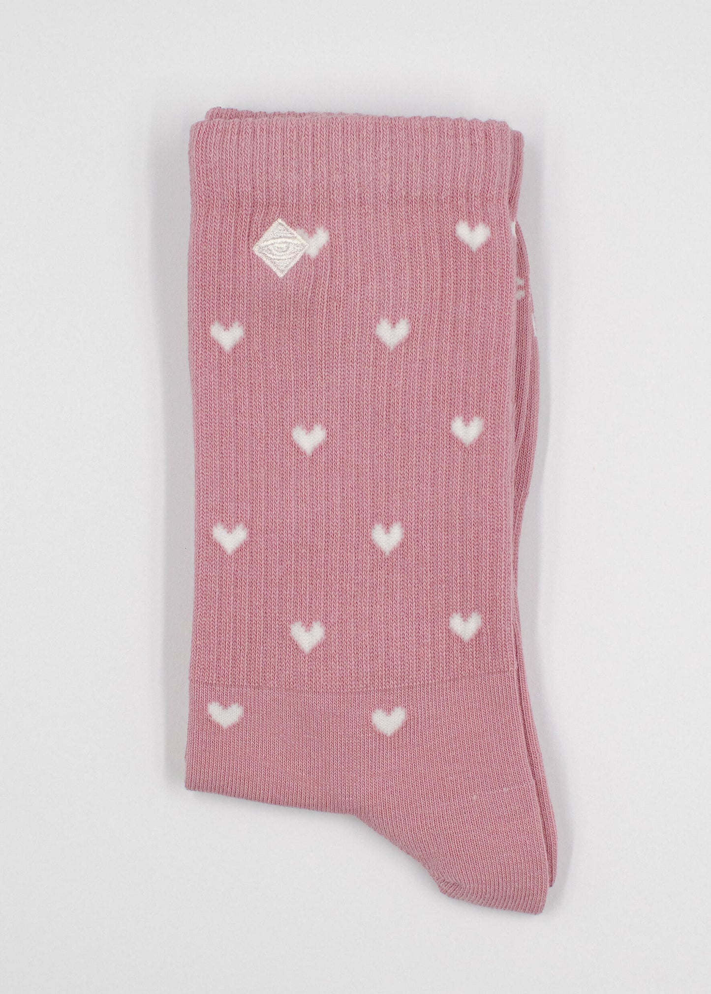 Ein Paar gefaltete rosafarbene J.Clay Tennissocken mit kleinen weißen Herzmustern und einem weißen Logo in der Nähe des oberen Randes, dargestellt auf einem schlichten weißen Hintergrund.