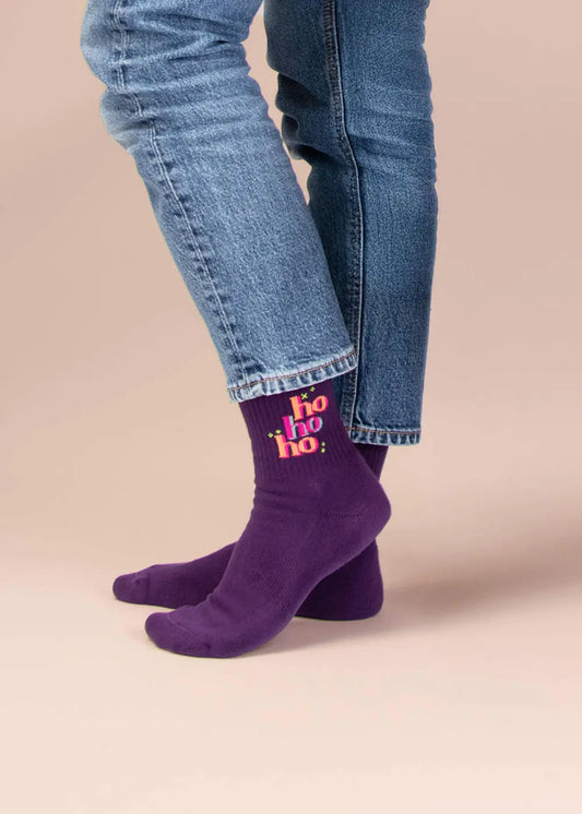 Die Person trägt J.Clay-„Ho ho ho“-Socken – ein lustiges Geschenk – unter hochgekrempelten Jeans.
