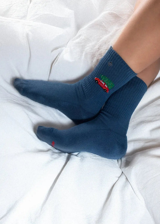 J.Clay „Driving Home for Christmas“-Socken – Motiv mit einer Person in einem roten Auto, die sich auf einem weißen Bett ausruht.