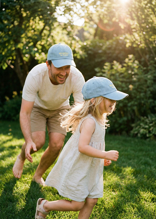 Ein Mann und ein Mädchen in J.Clay Breakfast in Paris - Kids Cap spielen zusammen auf einer sonnigen Wiese.