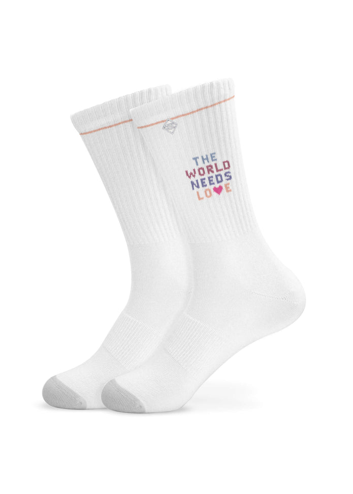 Ein Paar weiße J.Clay Tennissocken mit grauen Zehen und Absätzen, mit der Aufschrift "THE WORLD NEEDS LOVE" in bunten Blockbuchstaben und einem kleinen Herz unter dem Text.