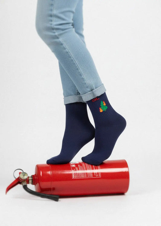 Person in blauen OH… Tannenbaum-Weihnachtssocken mit einem Baummotiv auf einem roten Feuerlöscher.