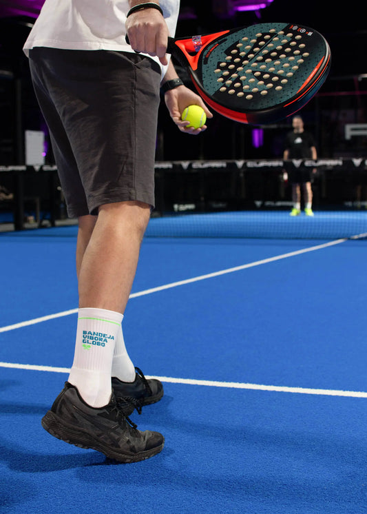 Abgebildet sind zwei weiße J.Clay-Socken mit grünen Akzenten und blauem "BANDEJA UNDERA GLOBO"-Schriftzug, ideal für Padel-Tennis-Fans. Das X SPORTS-Logo in Blau und Weiß ist in der oberen rechten Ecke abgebildet.