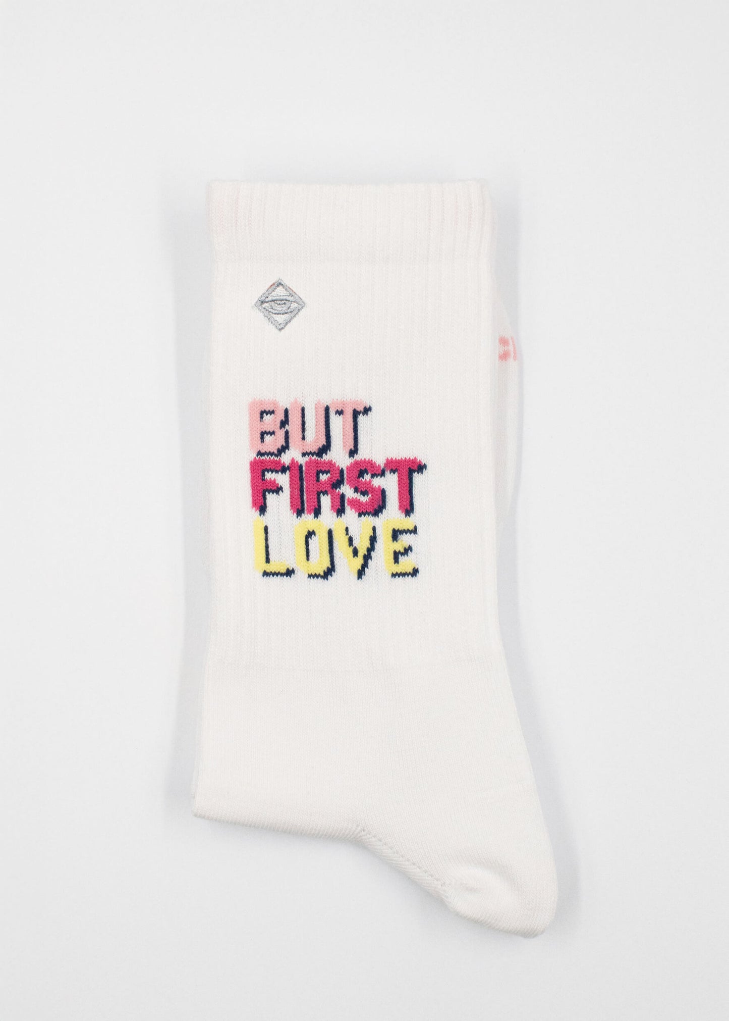 Ein Paar weiße J.Clay Tennissocken mit der Aufschrift "BUT FIRST LOVE" in fetten, bunten Buchstaben an der Seite.