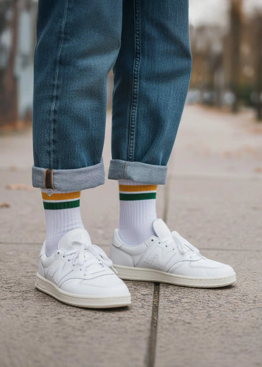 Eine Person mit Jeanshose und weißen New Balance Schuhen trägt die weißen Tennissocken mit orangen und grünen Streifen