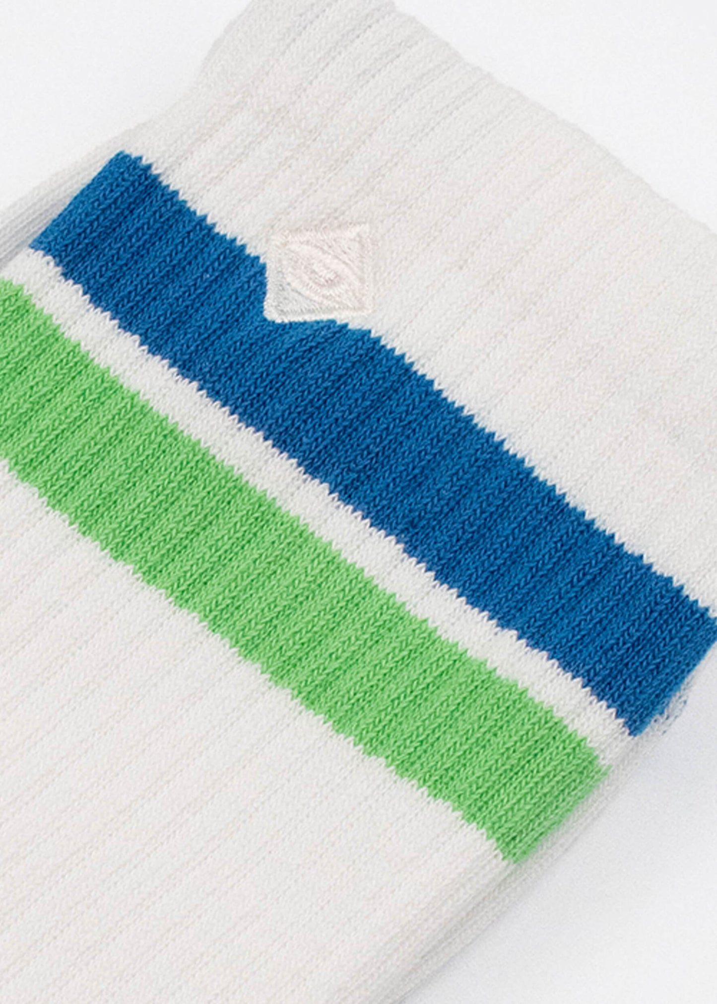 Eine Nahaufnahme einer weißen gerippten J.Clay-Tennissocke mit einem dicken blauen und einem dicken grünen Streifen und einem kleinen weißen gestickten Logo über den Streifen.