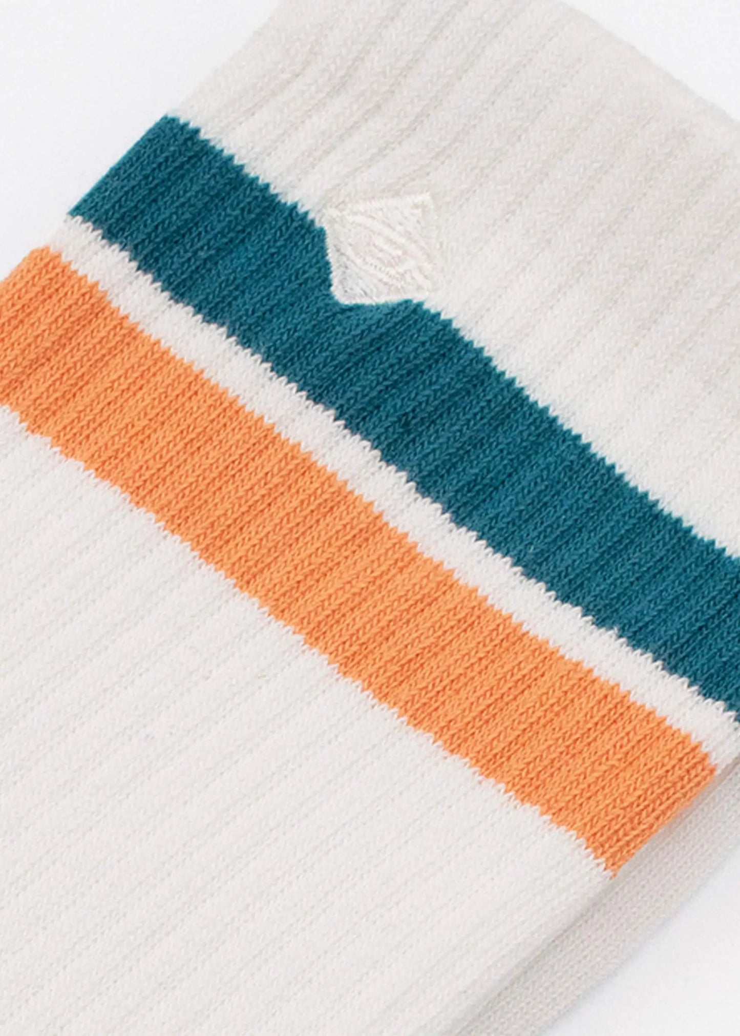 Eine Nahaufnahme einer weißen gerippten J.Clay-Tennissocke mit einem blaugrünen und einem orangefarbenen Streifen in der Nähe des oberen Randes sowie einer kleinen weißen gestickten Raute oberhalb der Streifen.