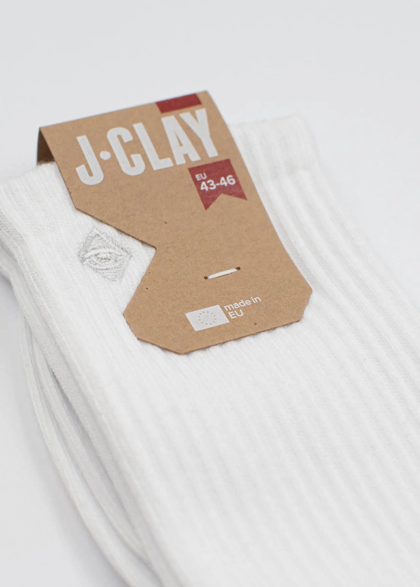 Ein Paar weiße gerippte Tennissocken von J.Clay, Größe EU 43-46, hergestellt in der EU. Sie verfügen über ein kleines gesticktes Logo in der Nähe der Oberseite und kommen mit einem braunen Karton-Tag für einen klassischen sportlichen Look.