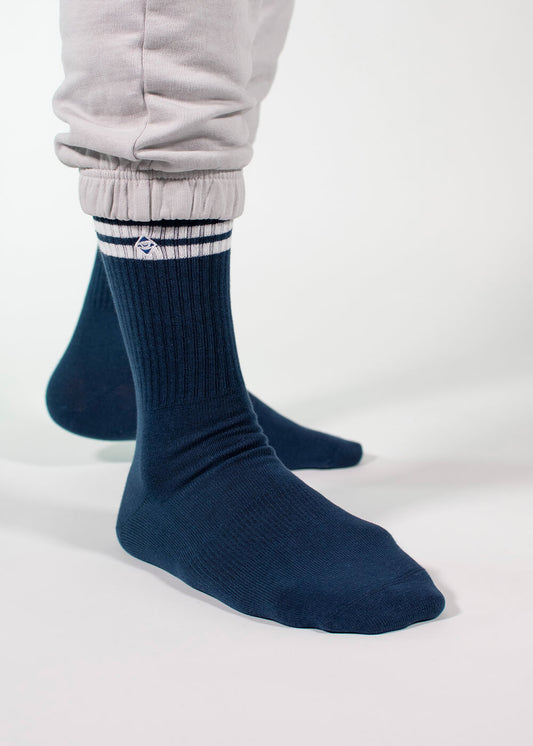 Eine Person, die eine hellgraue J.Clay-Jogginghose und eine dunkelblaue J.Clay-Tennissocke mit weißen Streifen in der Nähe des Oberteils trägt, steht vor einem weißen Hintergrund.