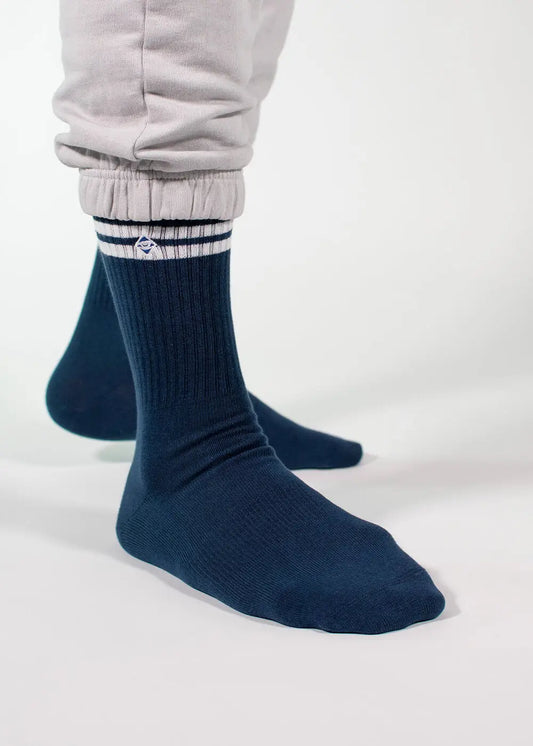 Eine Person, die eine hellgraue J.Clay-Jogginghose und eine dunkelblaue J.Clay-Tennissocke mit weißen Streifen in der Nähe des Oberteils trägt, steht vor einem weißen Hintergrund.