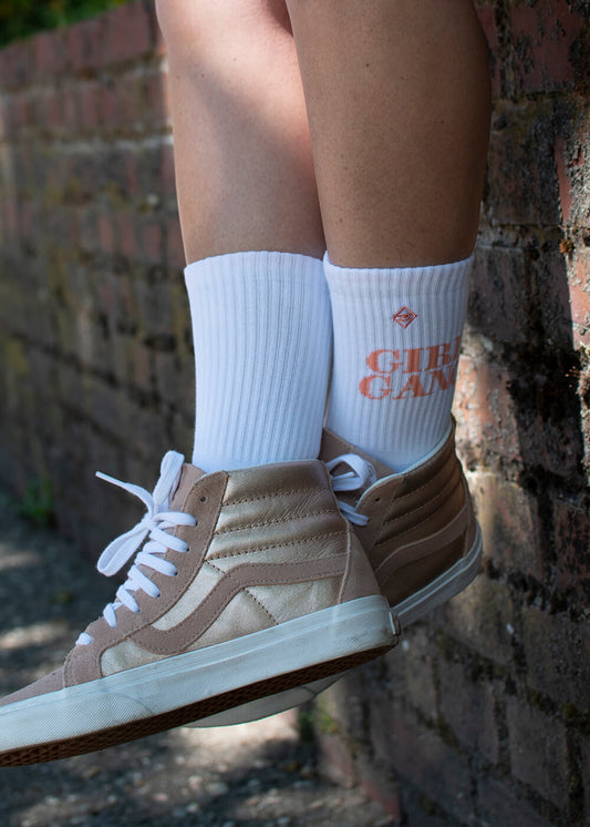 Ein Paar weiße J.Clay Tennissocken mit gerippten Bündchen, orangefarbenen Streifen in der Nähe der Zehen und einem orangefarbenen Aufdruck "GIRL GANG" an der Seite, abgebildet vor einem schlichten weißen Hintergrund. - Tennissocken